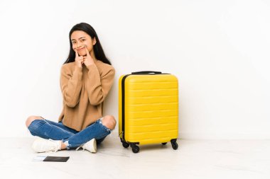 Genç Çinli gezgin kadın iki seçenek arasında şüpheyle izole edilmiş bir bavulla yerde oturuyor..