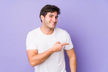 Mor arka planda izole edilmiş genç adam gülümsüyor ve boş alanda bir şeyler gösteriyor..