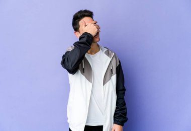 Mor arka planda izole edilmiş genç beyaz adam elleriyle gözlerini kapatıyor, geniş bir gülümsemeyle bir sürpriz bekliyor..