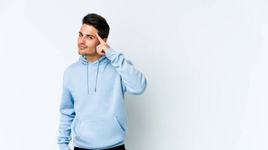 Beyaz arka planda izole edilmiş genç beyaz bir adam şakağı parmağıyla işaret ediyor, düşünüyor ve bir göreve odaklanıyor..