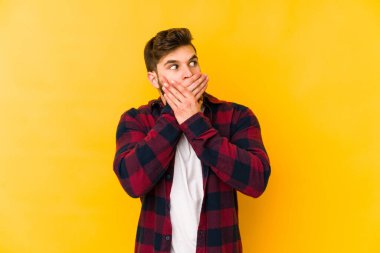 Kafkasyalı genç adam sarı arka planda izole edilmiş. Düşünceli bir şekilde, ağzını eliyle kapatan bir fotokopi odasına bakıyor..