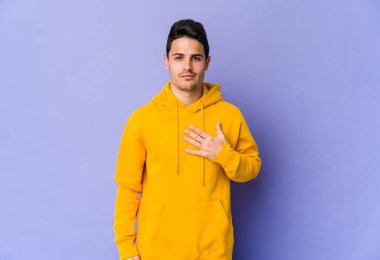 Mor arka planda izole edilmiş genç beyaz adam yemin ediyor, elini göğsüne koyuyor..