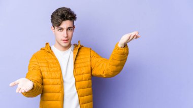 Mor arka planda izole genç beyaz adam kollarıyla ölçek yapar, mutlu ve kendinden emin hisseder..