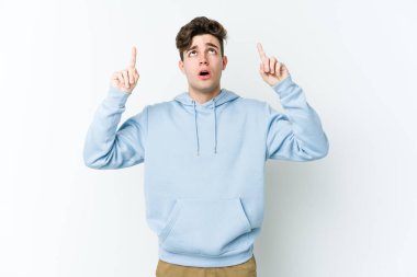 Beyaz arka planda izole edilmiş genç beyaz adam ağzı açık bir şekilde üst tarafı işaret ediyor..
