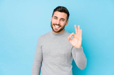 Mavi arka planda genç, beyaz bir adam yalnız, neşeli ve kendinden emin..