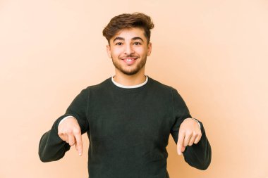 Bej arka planda izole edilmiş genç bir Arap, parmakları aşağıda, olumlu bir his var..