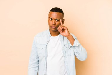 Genç Latin bir adam bej arka planda izole edilmiş. Parmağıyla tapınağı işaret ediyor. Düşünüyor, bir göreve odaklanıyor..