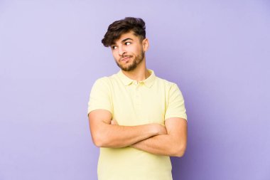 Mor arka planda izole edilmiş, hoşnutsuzca kaşlarını çatmış, kollarını kavuşturmuş genç bir Arap..