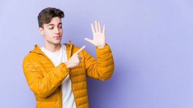Mor arka planda izole edilmiş genç beyaz adam gülümseyerek beş numarayı parmaklarıyla gösteriyor..