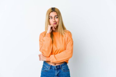 Beyaz arka planda izole edilmiş genç sarışın kadın şüpheli ve şüpheci bir ifadeyle yana bakıyor..