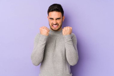 Mor arka planda izole edilmiş genç beyaz adam yumruğunu kameraya gösteriyor, agresif yüz ifadesi var..