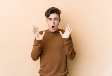 Beyazlı genç bir adam bej arka planda izole edilmiş. Şaşırmış ve şok olmuş..