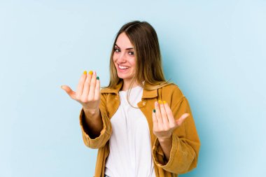 Mavi arka planda izole edilmiş genç beyaz kadın sanki seni davet ediyormuş gibi seni işaret ediyor..