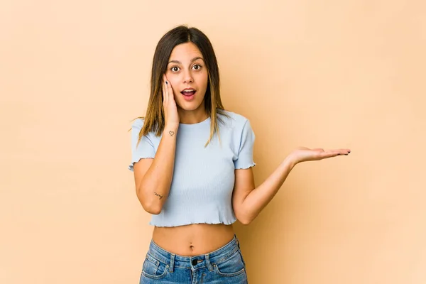 Mujer Joven Aislada Sobre Fondo Beige Impresionada Sosteniendo Espacio Copia — Foto de Stock