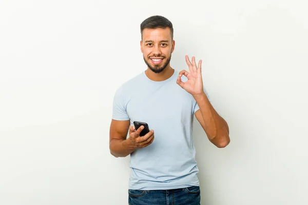 Jovem Mestiço Asiático Homem Segurando Telefone Alegre Confiante Mostrando Gesto — Fotografia de Stock