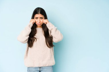 Genç Hintli bir kadın mavi arka planda yalnız başına sızlanıyor ve ağlıyor..