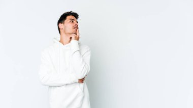 Beyaz arka planda izole edilmiş genç beyaz bir adam şüpheli ve şüpheci bir ifadeyle yana bakıyor..