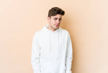 Beyazlı genç adam bej arka planda izole edilmiş omuzlarını silkeliyor ve gözleri açık..