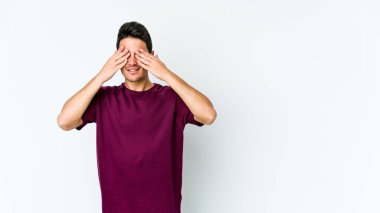 Beyaz arka planda izole edilmiş genç beyaz bir adam elleriyle gözlerini kapatmaktan korkuyor..