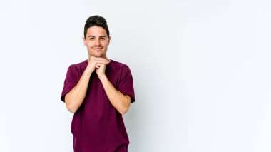 Beyaz arka planda izole genç beyaz adam ellerini çenesinin altında tutuyor, mutlu bir şekilde yana bakıyor..