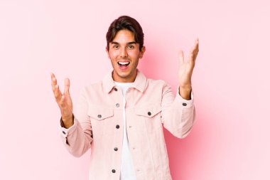 Pembe arka planda poz veren beyaz bir genç hoş bir sürprizle karşılaşıyor, heyecanlı ve el kaldırıyor..