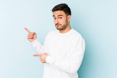 Mavi arka planda izole edilmiş genç beyaz adam işaret parmağıyla fotokopi alanını işaret ederek şok oldu..