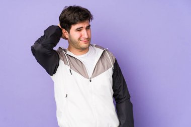 Mor arka planda soyutlanmış genç bir adam yorgun ve uykulu. Elini başının üstünde tutuyor..