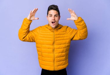 Mor arka planda izole olmuş genç beyaz bir adam zaferi ya da başarıyı kutluyor, şaşırıyor ve şok oluyor..