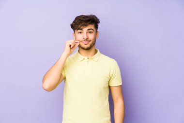 Mor arka planda izole edilmiş genç bir Arap adam parmakları dudaklarında bir sır saklıyor..