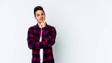 Beyaz arka planda izole edilmiş genç beyaz bir adam şüpheli ve şüpheci bir ifadeyle yana bakıyor..