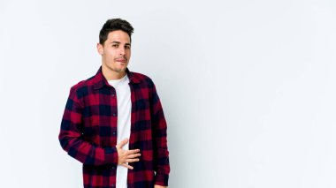 Beyaz arka planda izole edilmiş genç beyaz adam karnına dokunuyor, nazikçe gülümsüyor, yemek yiyor ve tatmin oluyor..