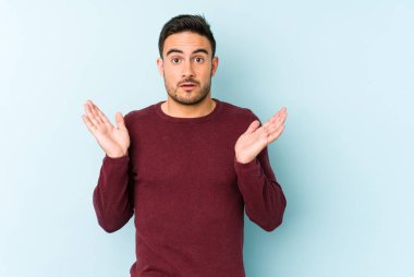 Kafkasyalı genç adam mavi arka planda izole edildi. Şaşırdı ve şok oldu..