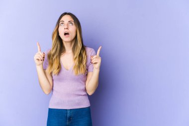 Mor arka planda izole edilmiş beyaz bir kadın ağzı açık bir şekilde üst tarafı işaret ediyor..