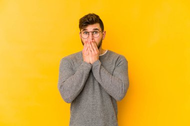Sarı arka planda izole edilmiş genç beyaz adam elleri endişeli bir şekilde ağzı örtüyor..