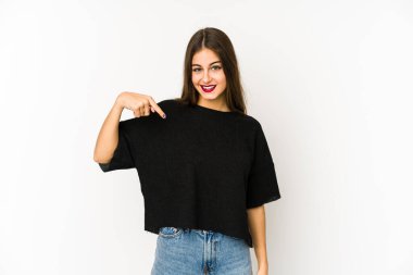 Beyaz arka planda yaşayan beyaz tenli genç bir kadın gömlek fotokopi alanını elle işaret ediyor, gururlu ve kendinden emin