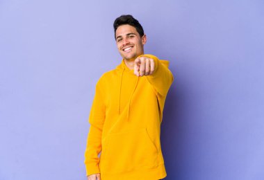 Mor arka planda izole edilmiş genç beyaz adam parmaklarıyla ön tarafı işaret ediyor..