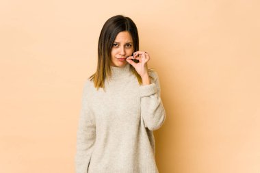 Bej arka planda izole edilmiş genç bir kadın, parmakları dudaklarında bir sır saklıyor..