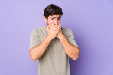 Mor arka planda izole edilmiş genç bir adam ağzını kapatıyor ve elleri endişeli görünüyor..