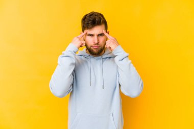 Sarı arka planda izole edilmiş genç beyaz adam bir göreve odaklanmış, işaret parmaklarını işaret ediyor..