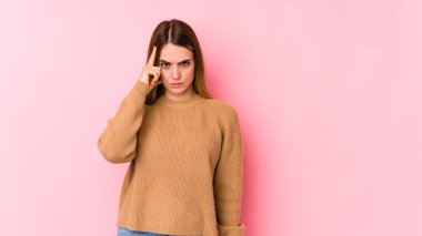 Pembe arka planda izole edilmiş beyaz bir kadın şakağı parmağıyla işaret ediyor, düşünüyor ve bir göreve odaklanıyor..