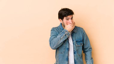 Genç adam bej arka planda izole edilmiş ağzını kapamış elleri endişeli görünüyor..
