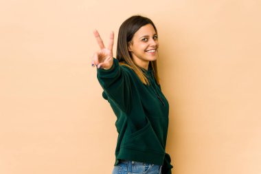 Bej arka planda izole edilmiş genç bir kadın neşeli ve kaygısız parmakları olan bir barış sembolü gösteriyor..