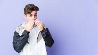 Mor arka planda izole edilmiş genç beyaz adam elleriyle ağzını kapatırken şok oldu..