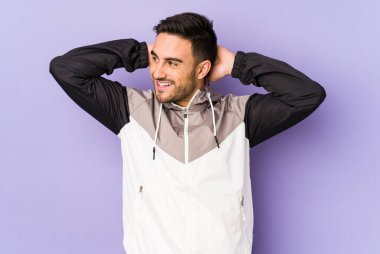 Mor arka planda izole olmuş genç beyaz bir adam kendini güvende hissediyor, elleri başının arkasında..