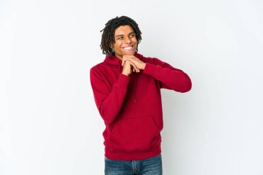 Genç Afrikalı Amerikalı Rasta adam ellerini çenesinin altında tutuyor ve mutlu bir şekilde yan tarafa bakıyor..