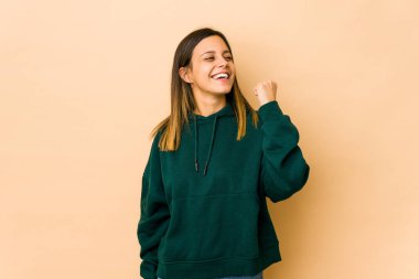 Bej arka planda izole edilmiş genç bir kadın zaferi, tutkuyu ve coşkuyu, mutlu ifadeyi kutluyor..