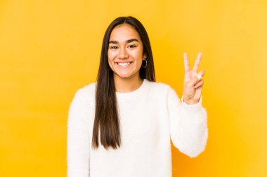 Sarı arka planda izole edilmiş genç bir kadın zafer işareti gösteriyor ve gülümsüyor..