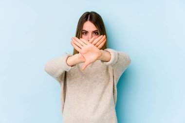 Mavi arka planda izole edilmiş genç beyaz bir kadın inkar jesti yapıyor.