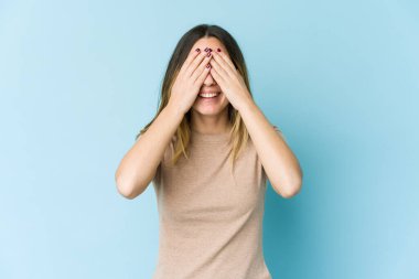 Mavi arka planda soyutlanmış beyaz bir kadın elleriyle gözlerini kapatıyor, gülümseyerek bir sürpriz bekliyor..