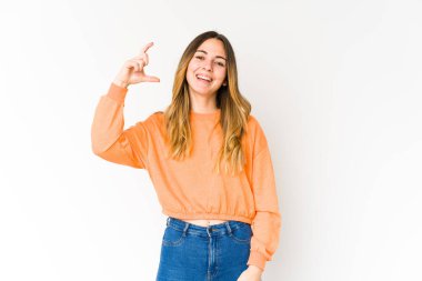 Beyaz arka planda izole edilmiş genç beyaz bir kadın. Elinde parmakları olan, gülümseyen ve kendinden emin bir şey tutuyor..